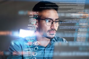 Man wearing glasses studies lines of code on a transparent screen, symbolizing cybersecurity and attack-surface discovery—an offensive-security service powered by CyberGrant